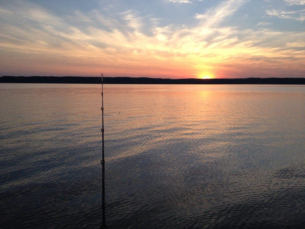 A fishing rod set up beside a lake at sunset